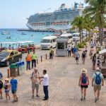 Tourists walk along a Mexican cruise port waterfront with a large cruise ship docked, as Mexico reports record international visitor numbers through July 2026.